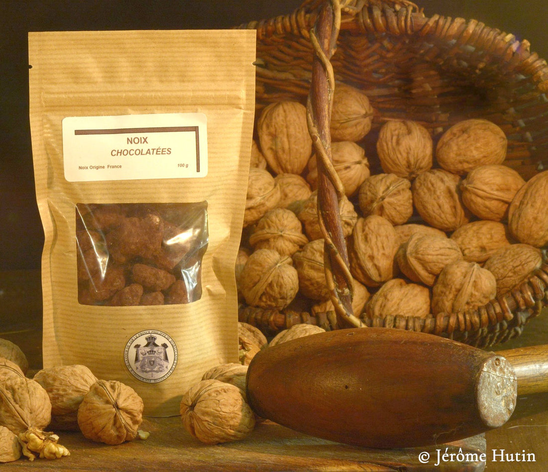 Sachet de cerneaux de noix au chocolat noir devant un panier de noix