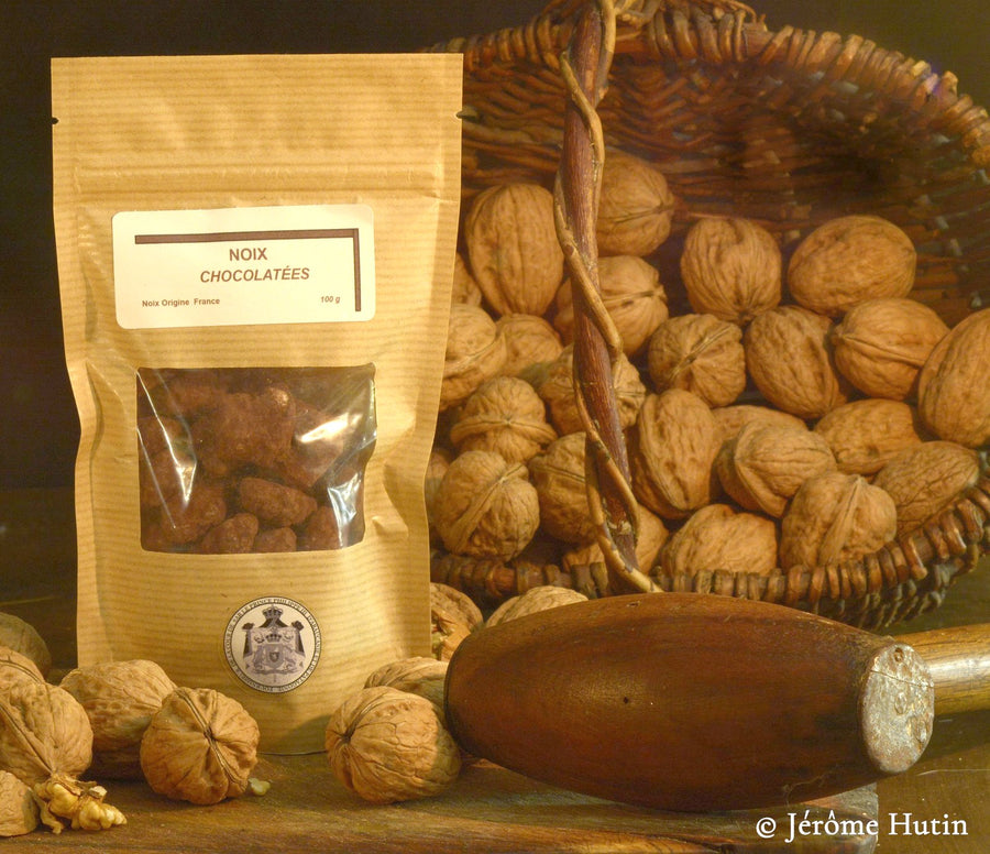 Sachet de cerneaux de noix au chocolat noir devant un panier de noix